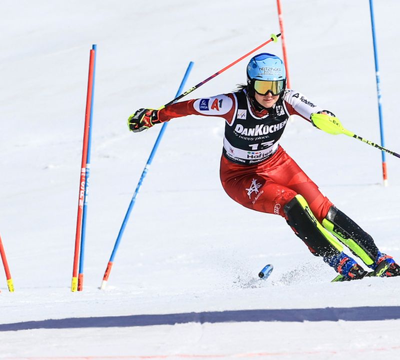 Skirennläuferin in rotem Anzug beim dynamischen Slalomlauf auf Schnee, umgeben von blauen und roten Toren.