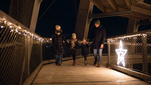 Family walking at night along an illuminated wooden walkway decorated with fairy lights and glowing star decorations.