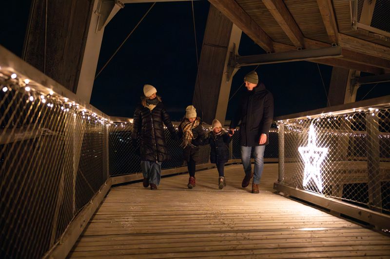 A family walking along an illuminated wooden footpath at night, decorated with fairy lights and glowing star decorations.