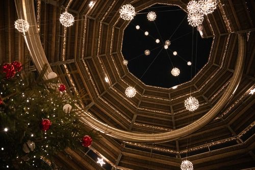 Interior shot of a round illuminated tower at night surrounded by brightly lit Christmas baubles and, on the left of the picture, the top of a decorated Christmas tree.