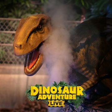 Close-up of a roaring dinosaur animatronic with "Dinosaur Adventure Live" logo at the bottom, surrounded by foliage.