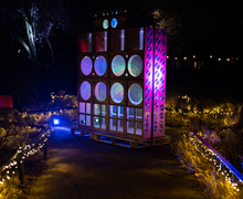 A large, illuminated outdoor art installation with colorful circular lights, surrounded by pathways lined with string lights at night.