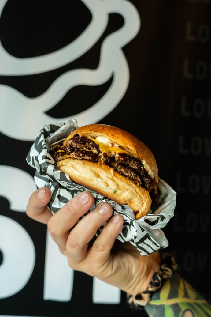 Hand holding a wrapped burger with melted cheese and a toasted bun, set against a dark abstract background.