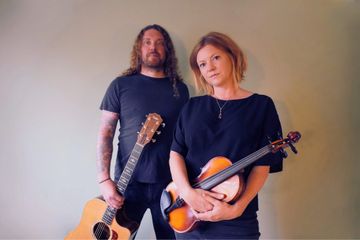 2 artists stand looking into camera with musical instruments in hand