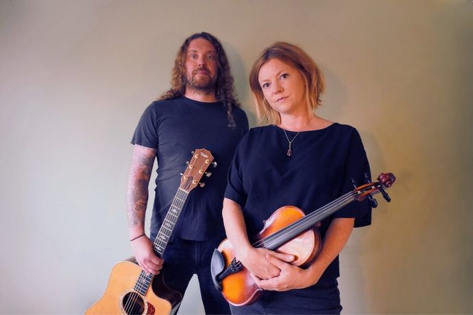 2 artists stand looking into camera with musical instruments in hand