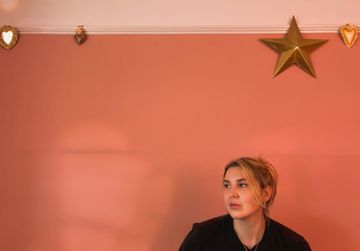 Person sitting indoors against a pink wall decorated with a gold star and small heart-shaped ornaments.