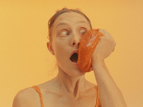 Yellow background with person looking shocked holding orange shiny squishy object to cheek