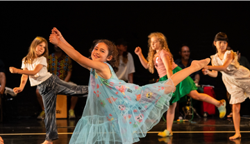 Children perform an energetic dance on a stage, wearing colourful outfits and striking dynamic poses.