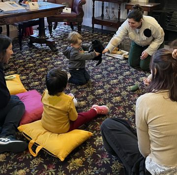 Children sit in a circle as a toddler gently holds a small black animal indoors.