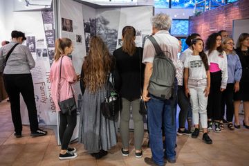 people stand around display exhibition boards with the word romania on it. people of mixed ages from teenager to older
