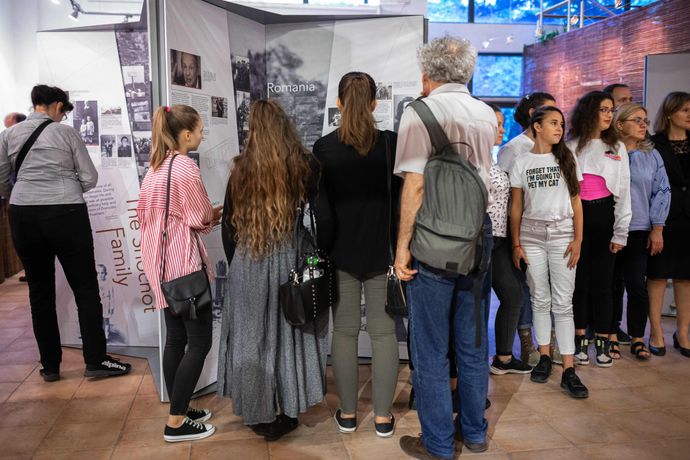 people stand around display exhibition boards with the word romania on it. people of mixed ages from teenager to older
