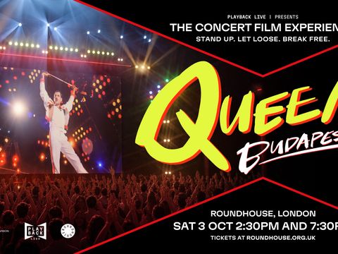 Large crowd watches concert film screening with bright stage lights, giant screen, and event promotion.