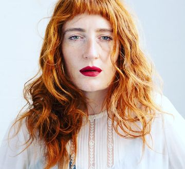 A close-up portrait of a person with long wavy hair, wearing a light-colored top, against a plain background. Provide your feedback on BizChat