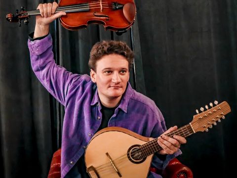 person wearing purple shirt holds two string instruments, one holding above head