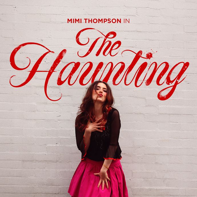 Person with long hair in a black top and bright pink skirt stands against a white brick wall, with large red script text reading 'The Haunting' above.