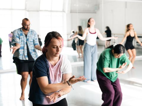 People practicing dance or movement exercises in a bright studio, focusing on their motions and expressions.