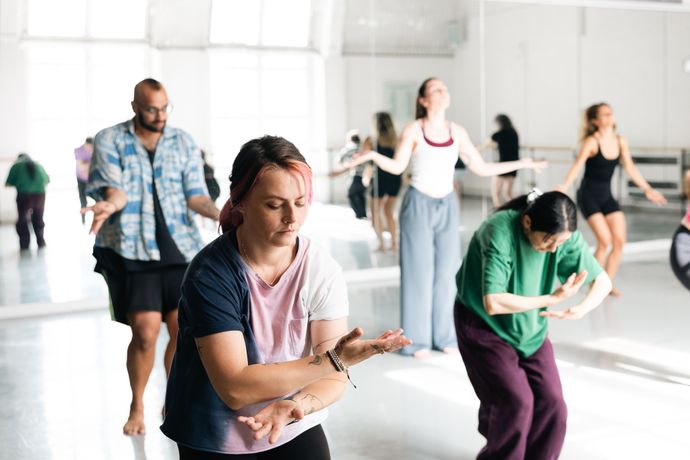 People practicing dance or movement exercises in a bright studio, focusing on their motions and expressions.