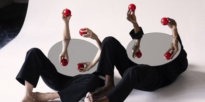 2 people lay on the ground. Their faces covered with mirrors and their hands each hold red mini balls