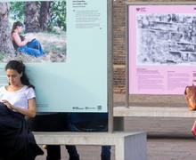 Person sits on concrete bench while leaning against artwork stand