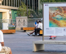 Person sits looking at artwork on stand above concrete bench in granary square