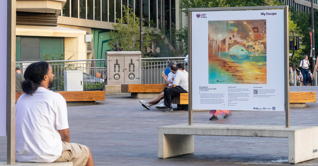 Person sits looking at artwork on stand above concrete bench in granary square