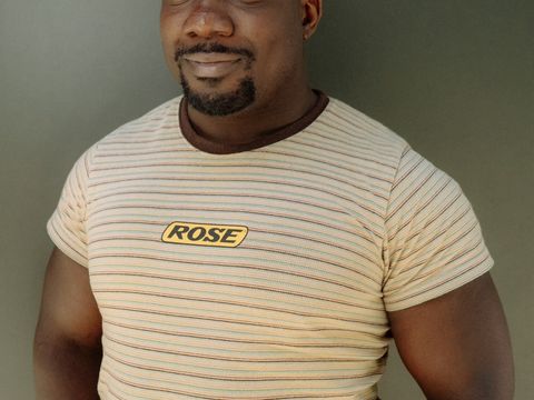 Person smiles to camera, wearing beige t shirt with red and blue thin stripes