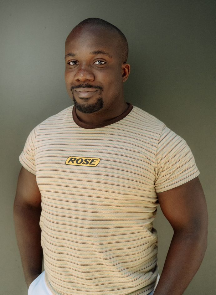 Person smiles to camera, wearing beige t shirt with red and blue thin stripes