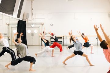 A group of people in a dance studio practicing dynamic poses with outstretched arms and bent knees.