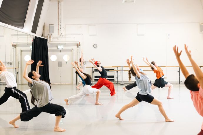 A group of people in a dance studio practicing dynamic poses with outstretched arms and bent knees.