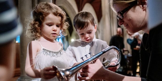 Two children examining a brass instrument with an adult in an indoor performance venue.