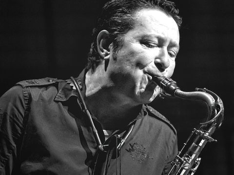 A musician passionately playing a tenor saxophone, his eyes closed, wearing a dark shirt, captured in a black and white photograph.