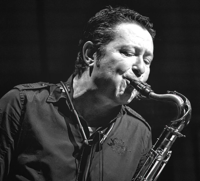 A musician passionately playing a tenor saxophone, his eyes closed, wearing a dark shirt, captured in a black and white photograph.