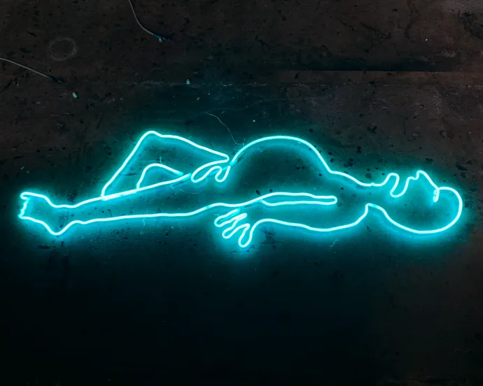 Neon outline of a reclining human figure glowing in blue against a dark background.
