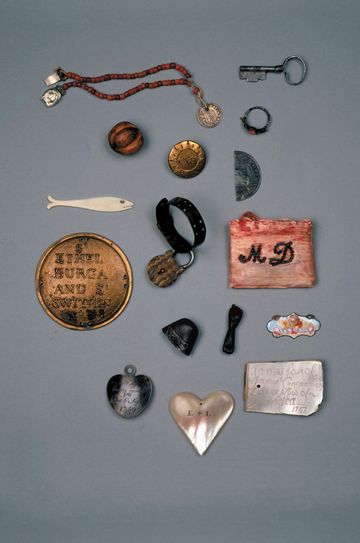 Collection of antique personal keepsakes, coins, jewelry, keys, and engraved tokens neatly arranged on gray background.