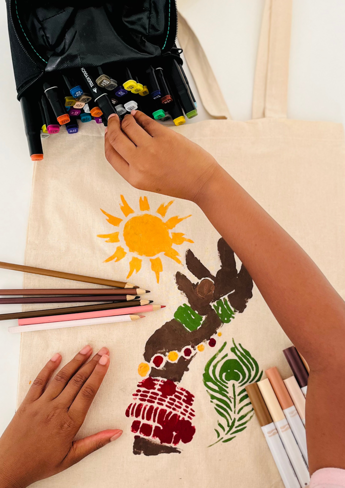 Child decorating a canvas bag with colorful markers and pencils, featuring a sun and abstract designs.