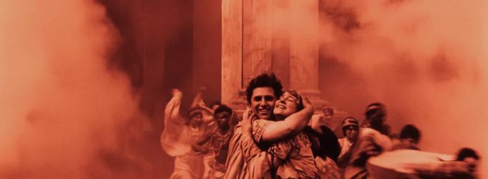 A joyous couple embraces in the foreground, surrounded by swirling orange smoke and chaotic movement in a historical setting.