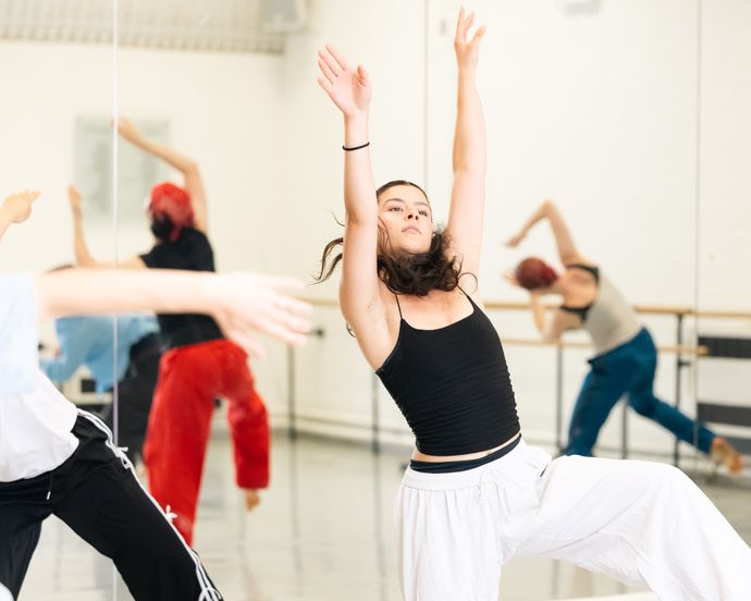 People dancing energetically in a studio with mirrors, wearing casual dance attire, including tank tops and loose pants.