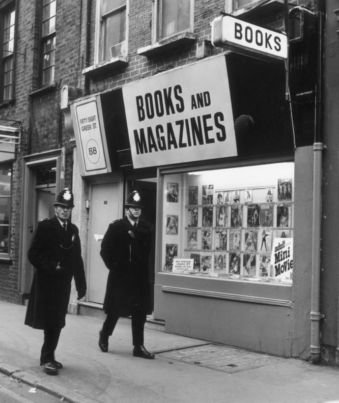2 policemen walk in front of a shop called 'Books and Magazines'