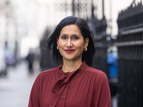Woman smiles to camera wearing burgundy top and gold earrings