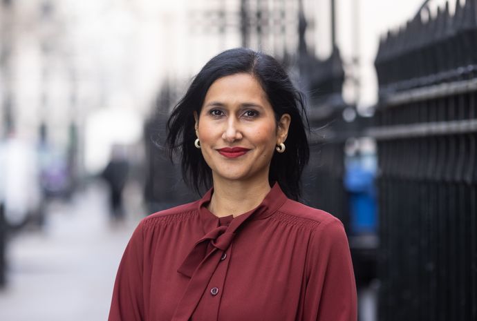 Woman smiles to camera wearing burgundy top and gold earrings