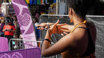 Performer with a microphone on stage, facing a crowd. A purple banner with a heart design is visible in the background.
