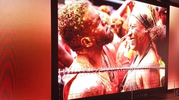 A joyful man and woman covered in colorful paint smile at each other, surrounded by a vibrant, festive atmosphere.