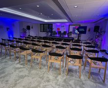 A large empty meeting room with rows of moveable chairs and a screen at the front