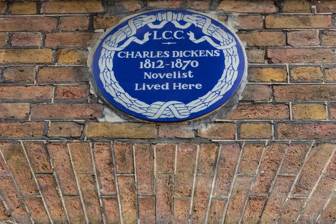 A blue circular plaque on a brick wall stating that the novelist Charles Dickens lived at this location.