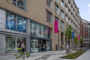 Modern brick building with large windows and "City Lit" signage, people entering and exiting, trees lining the sidewalk.