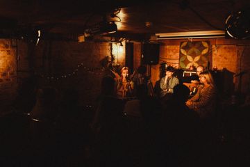 Intimate live music performance in a dimly lit, rustic venue with four musicians, surrounded by a cozy audience.