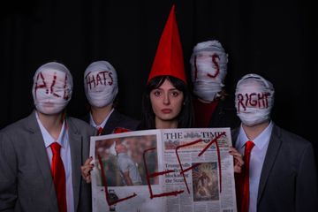 Five people hold a marked newspaper, some with bandaged faces and red accents, against a dark background.