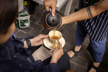 One person holding a ta cup whilst the other pours it with tea