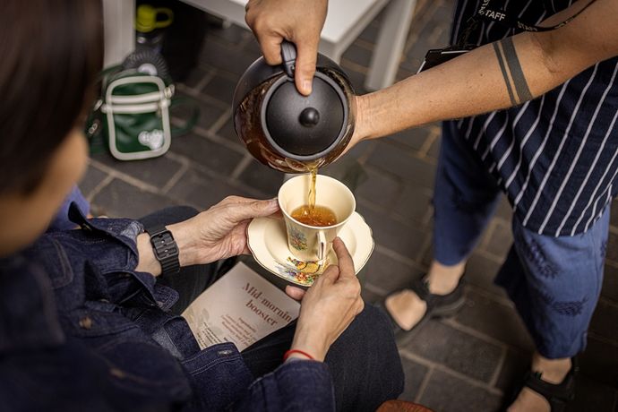 One person holding a ta cup whilst the other pours it with tea