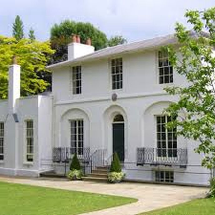 Elegant white two-story house with large windows, green front door, small porch, and well-maintained lawn, surrounded by lush greenery.